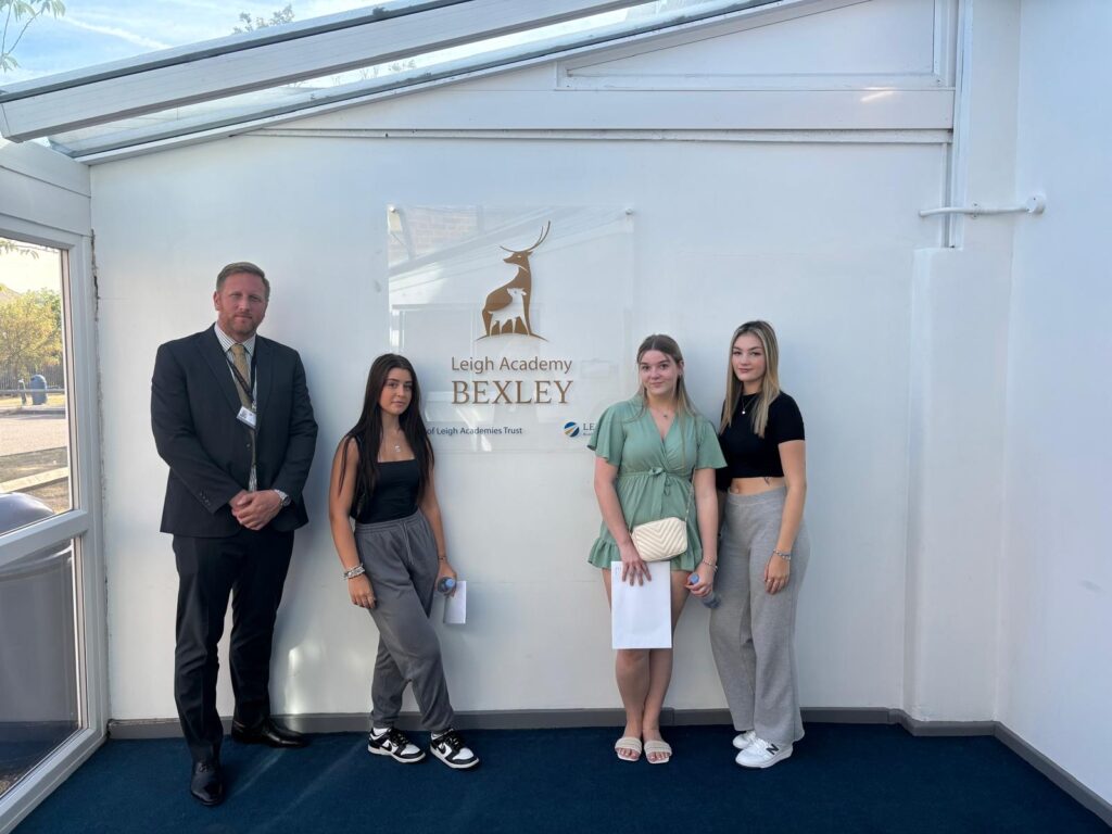 Three female Post-16 students are pictured smiling for the camera together with their Principal, after having just opened their A-Level results.