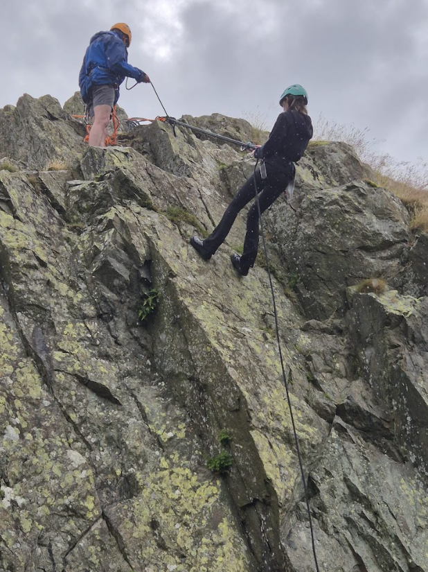One person abseiling down a cliff while another person holds onto the rope