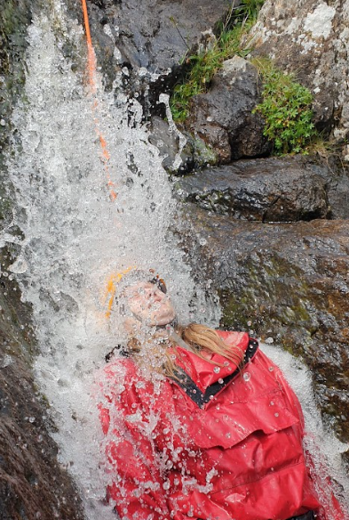 Someone wearing a helmet and wearing wet weather clothes under a waterfall
