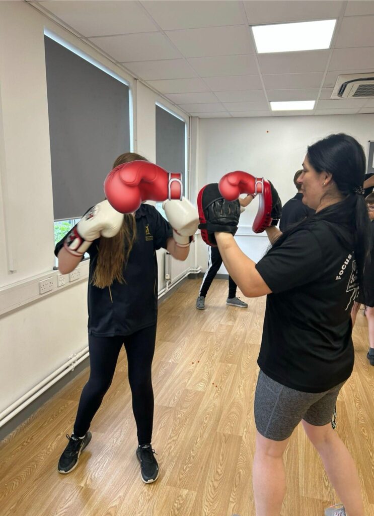 Pupils in PE kits receive boxing lessons in a room with wooden flooring