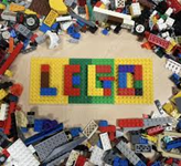 A top-down shot of a large pile of various colored and shaped LEGO bricks scattered around the edge of the frame. In the center, the word "LEGO" is spelled out clearly using large, rectangular bricks of yellow, red, green, and blue.
