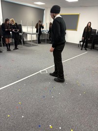 A man and students look at a small object on a dotted carpet.