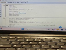 A close-up shot of a laptop screen showing a Python coding environment with various "import" statements and variable definitions visible.