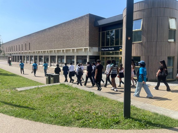 A group of students walking along a paved pathway outside a large campus building labeled "Marlowe North" on a clear, sunny day.